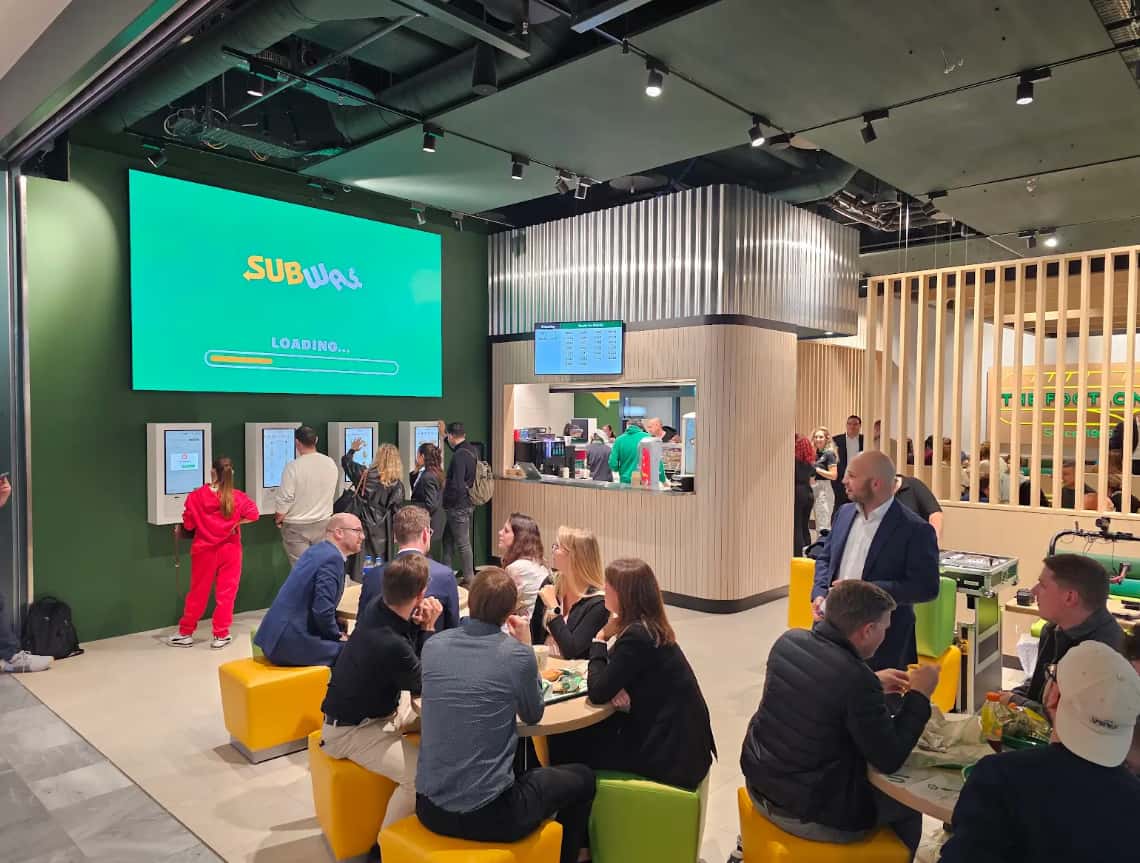 A Subway restaurant interior integrating technology with self-service kiosks for ordering, a vibrant design theme, and a welcoming customer experience.