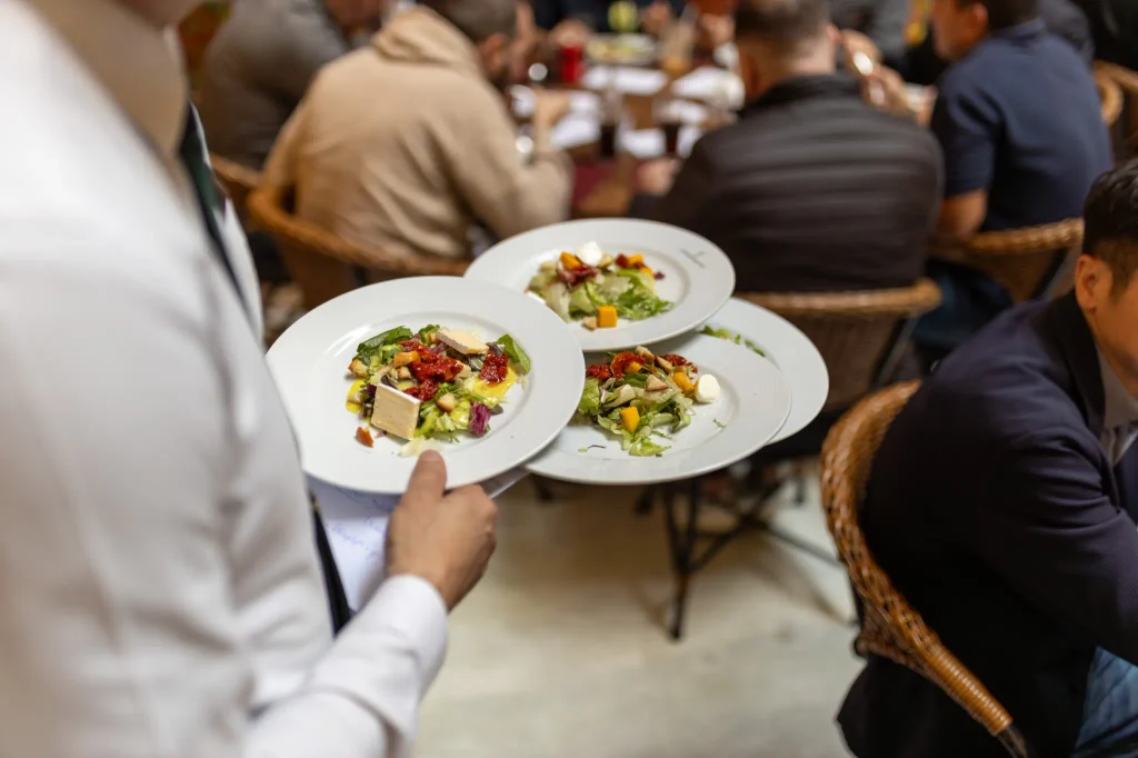 Waiter carrying several plates through a busy restaurant dining room